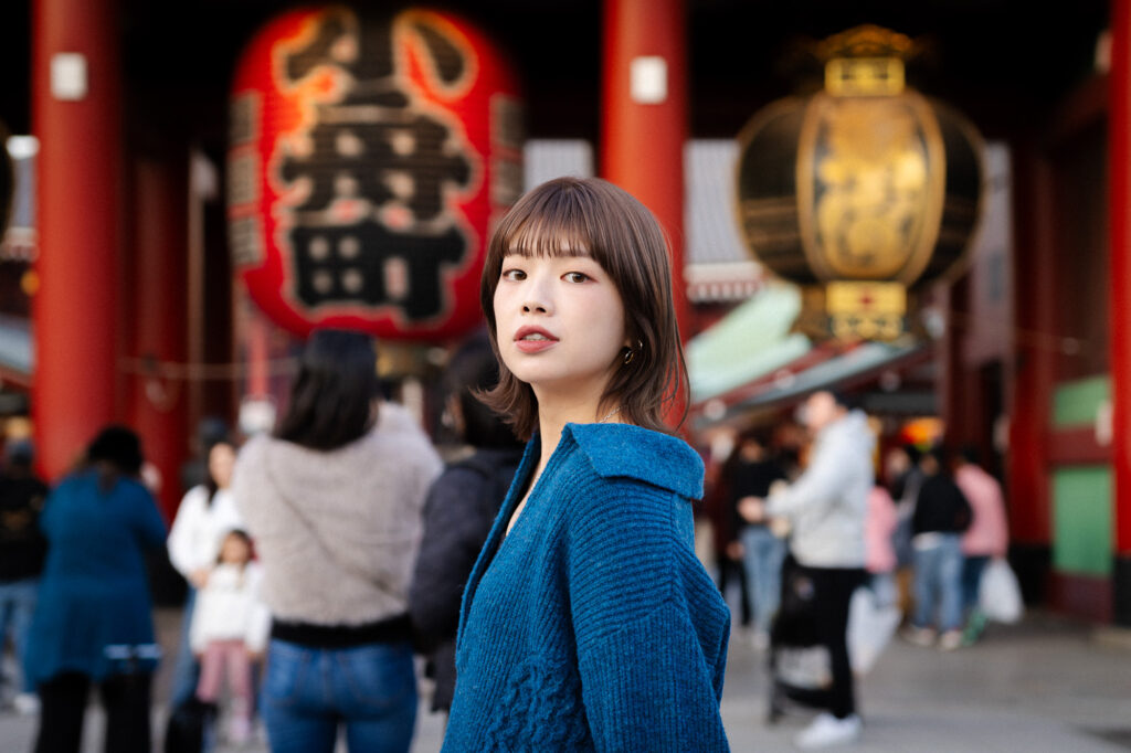 Portrait in Sensoji Temple in Asakusa A woman in a blue sweater stands in front of Sensoji Temple entrance in Asakusa with large lanterns and red decorations.