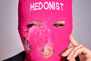 JG Studio Model Lua for the Japanese Brand Hedonist A Tokyo model wearing a pink balaclava with the word "Hedonist" and blowing smoke.