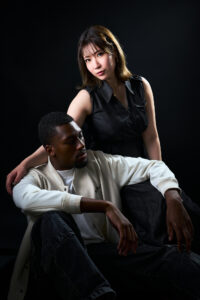 Japanese Model Chitose Yuki A couple in a studio portrait, with a famous Japanese actress standing and the man sitting, both dressed in contrasting outfits.