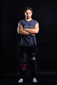 Fitness Portrait for a Model Portfolio by JG Brasseur Portrait of a man with tattooed arms in a black sleeveless shirt and patched black pants, studio photography by JG Brasseur.