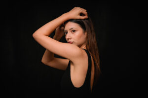 Studio Portrait of French Influencer Ines Arjoun by JG Brasseur Portrait of a woman with long hair in a black sleeveless top, posing with arms raised, studio photography by JG Brasseur.