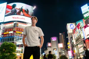 Exploring Shibuya Scramble Crossing at Night: Tokyo Photo Tour Young man at Shibuya Scramble Crossing at night, surrounded by neon signs and billboards during a Tokyo photo tour.
