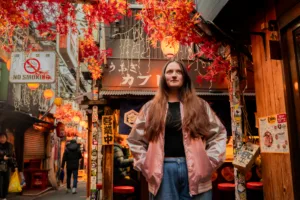 Autumn in Tokyo: Street Fashion in a Traditional Alley Person posing in a Tokyo alley decorated with autumn leaves and lanterns, wearing a shiny pink jacket.