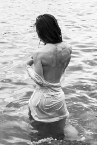 Fine art portrait of a person in water, draped in white fabric, evoking tranquility and connection with nature. Black and white photography.