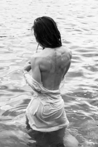 静かなる瞬間:水辺で瞑想する女性、自然写真 透き通った布をまとった女性が浅瀬に座り、静けさと自然との調和を感じさせる写真。