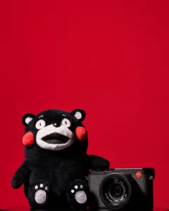 Kumamon, the popular Japanese mascot, posing with a Leica camera, showcasing product photography in Tokyo.