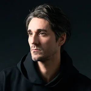 Self-Portrait of JG Brasseur | Tokyo Photographer Professional portrait of photographer JG Brasseur wearing a black hoodie, featuring dramatic low-key lighting and a dark background.